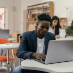 Grupo diverso de estudantes universitários usando laptops e estudando em uma sala de aula moderna.