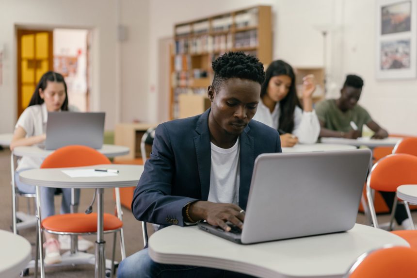 Grupo diverso de estudantes universitários usando laptops e estudando em uma sala de aula moderna.