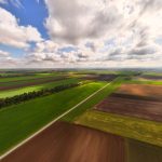 Vista aérea de extensas áreas agrícolas sob céu parcialmente nublado.