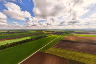 Vista aérea de extensas áreas agrícolas sob céu parcialmente nublado.