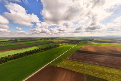 Vista aérea de extensas áreas agrícolas sob céu parcialmente nublado.