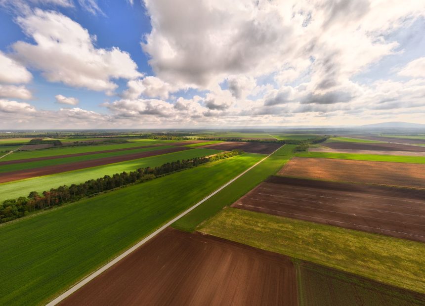 Vista aérea de extensas áreas agrícolas sob céu parcialmente nublado.