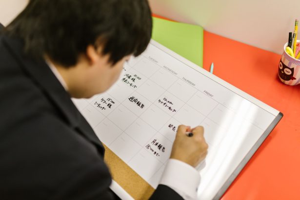Pessoa organiza um planejamento semanal em uma agenda sobre a mesa de trabalho.